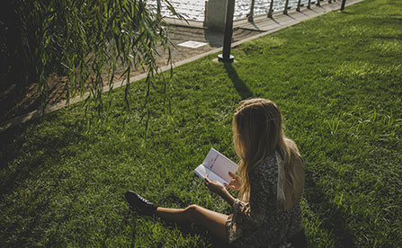 Person reading a book in a park, sitting on grass